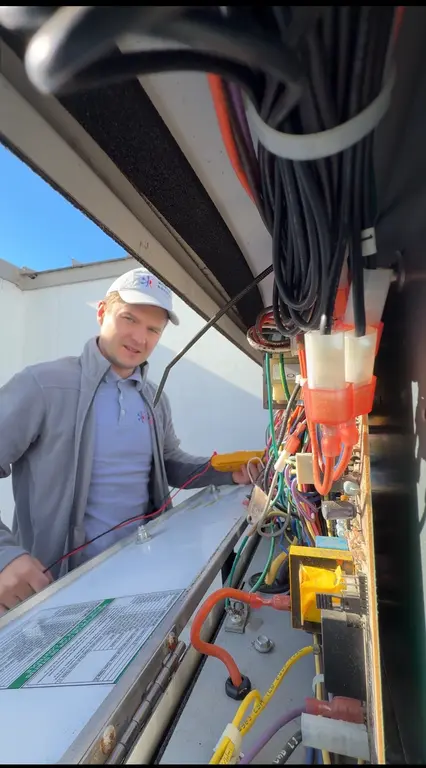 North Breeze technician testing electrical with multimeter inside RTU